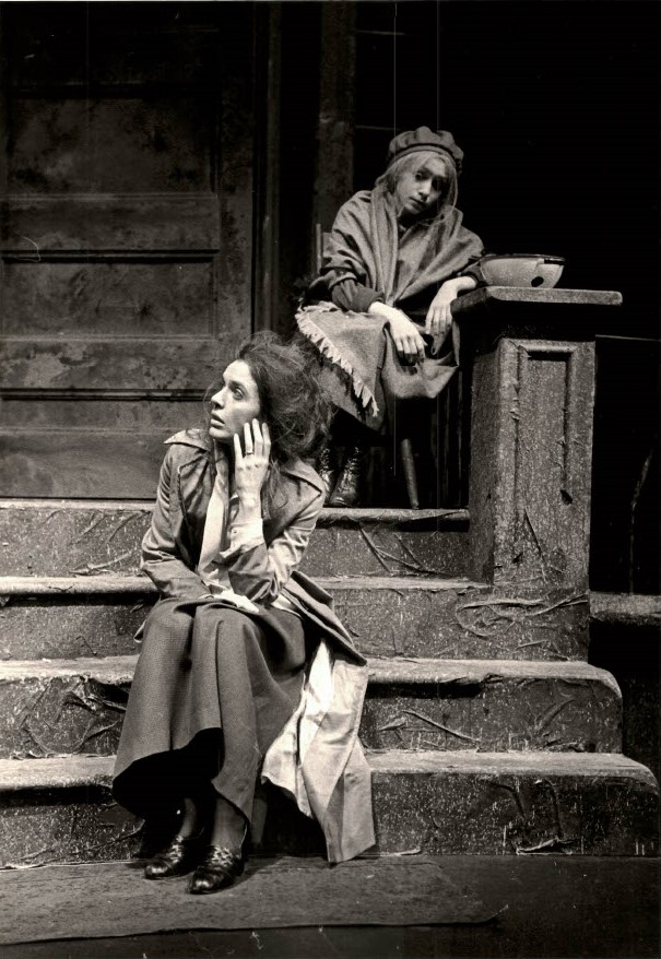 An image of young Deborah Kipp onstage. She is dressed in rags, has disheveled hair, and sits at the bottom of a staircase.