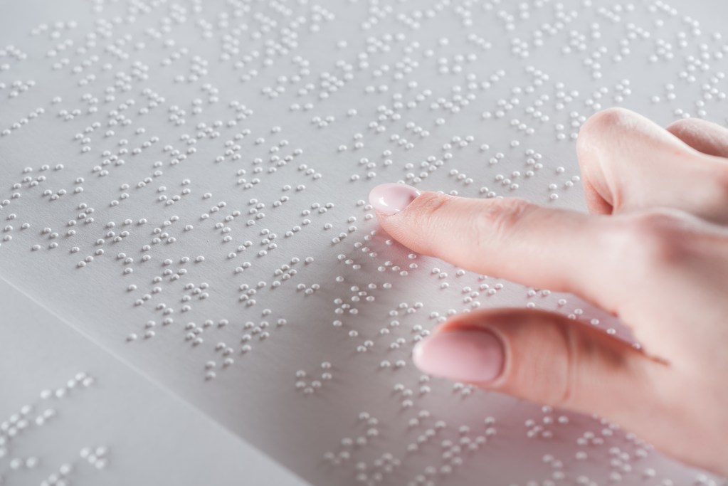 A closeup image of a woman’s hands reading a braille book