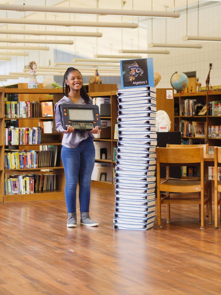 A young student with low vision holds up the Monarch tactile device in a school library.